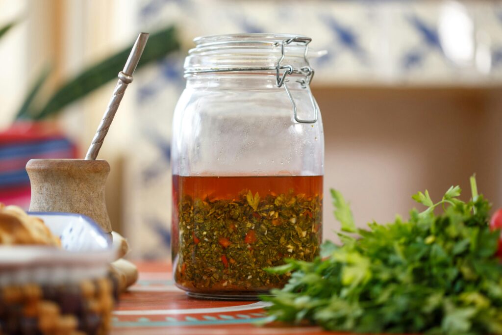 A glass jar filled with vibrant chimichurri sauce surrounded by fresh herbs, ready for a culinary delight.
